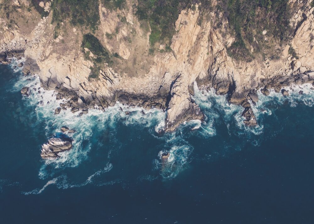 Aerial view of a rocky coastline with waves crashing against cliffs and deep blue ocean