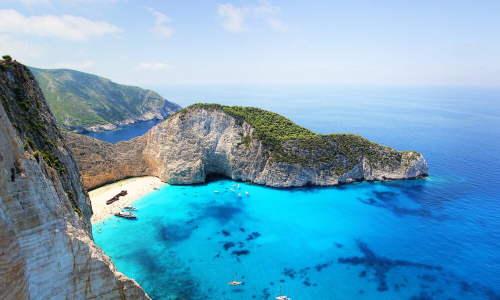 Aerial view of a turquoise cove with steep limestone cliffs, a small sandy beach and several boats
