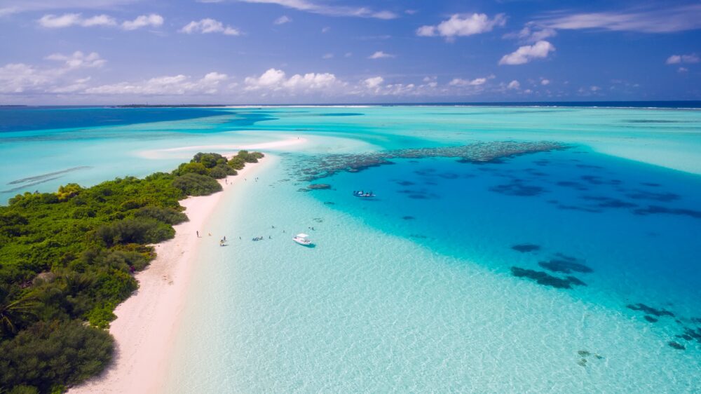 Aerial view of a white sandbar, turquoise lagoon, green island vegetation, and small boats